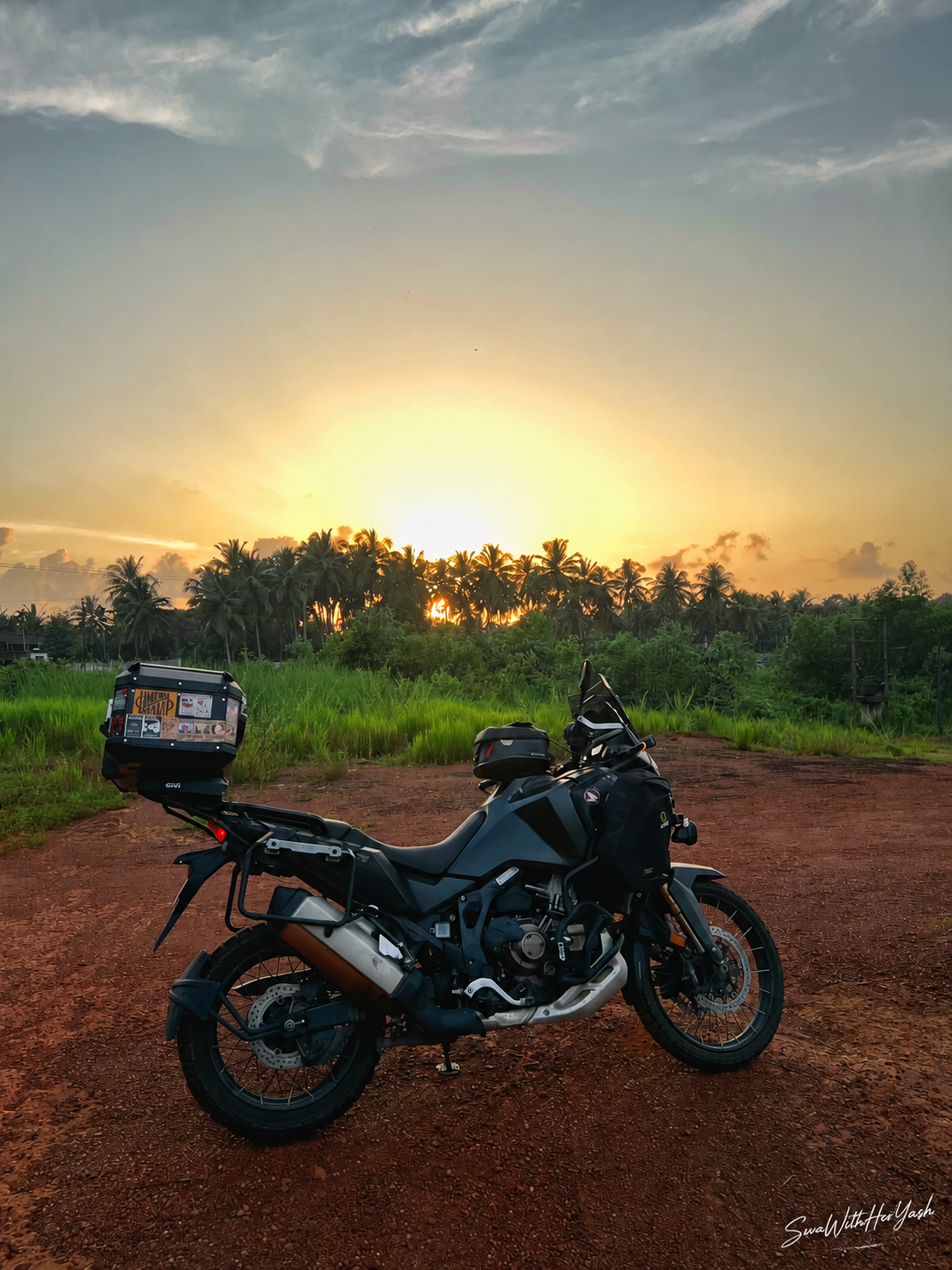 A superbike resting on a Mangalorean red-earth road at sunset, surrounded by coconut palms and lush green fields.